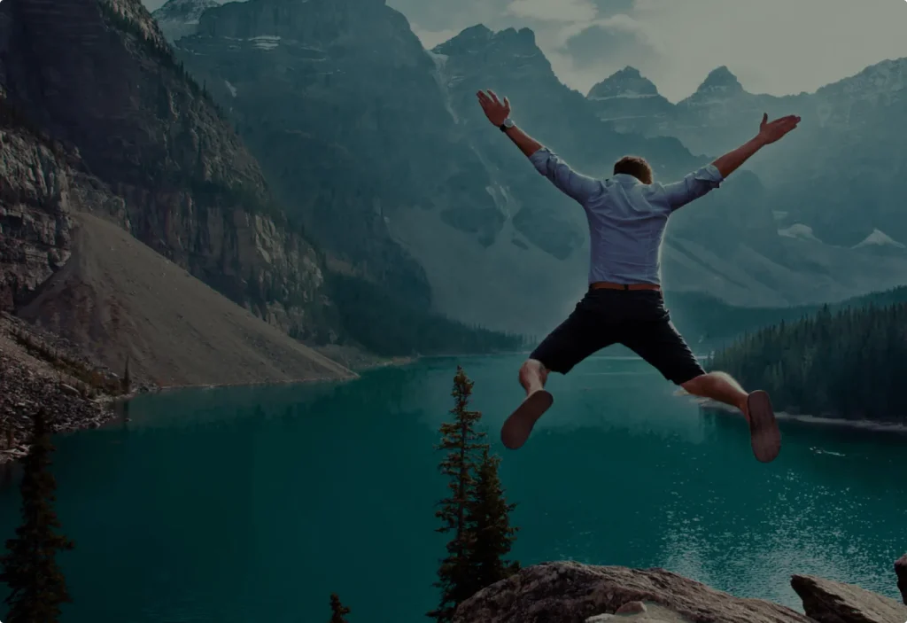 A man joyfully jumping in front of a stunning mountain lake.