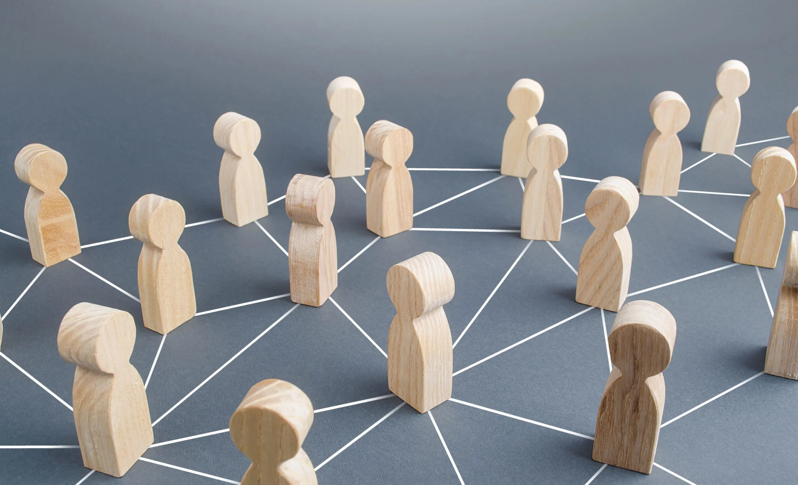 Wooden figurines stand on a dark surface, connected by white lines forming a network, symbolizing social or professional connections and communication within a community.