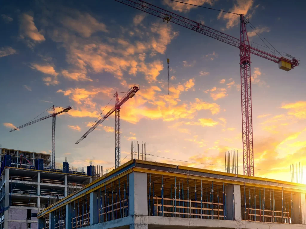 A construction site at sunset with cranes and clouds in the sky.