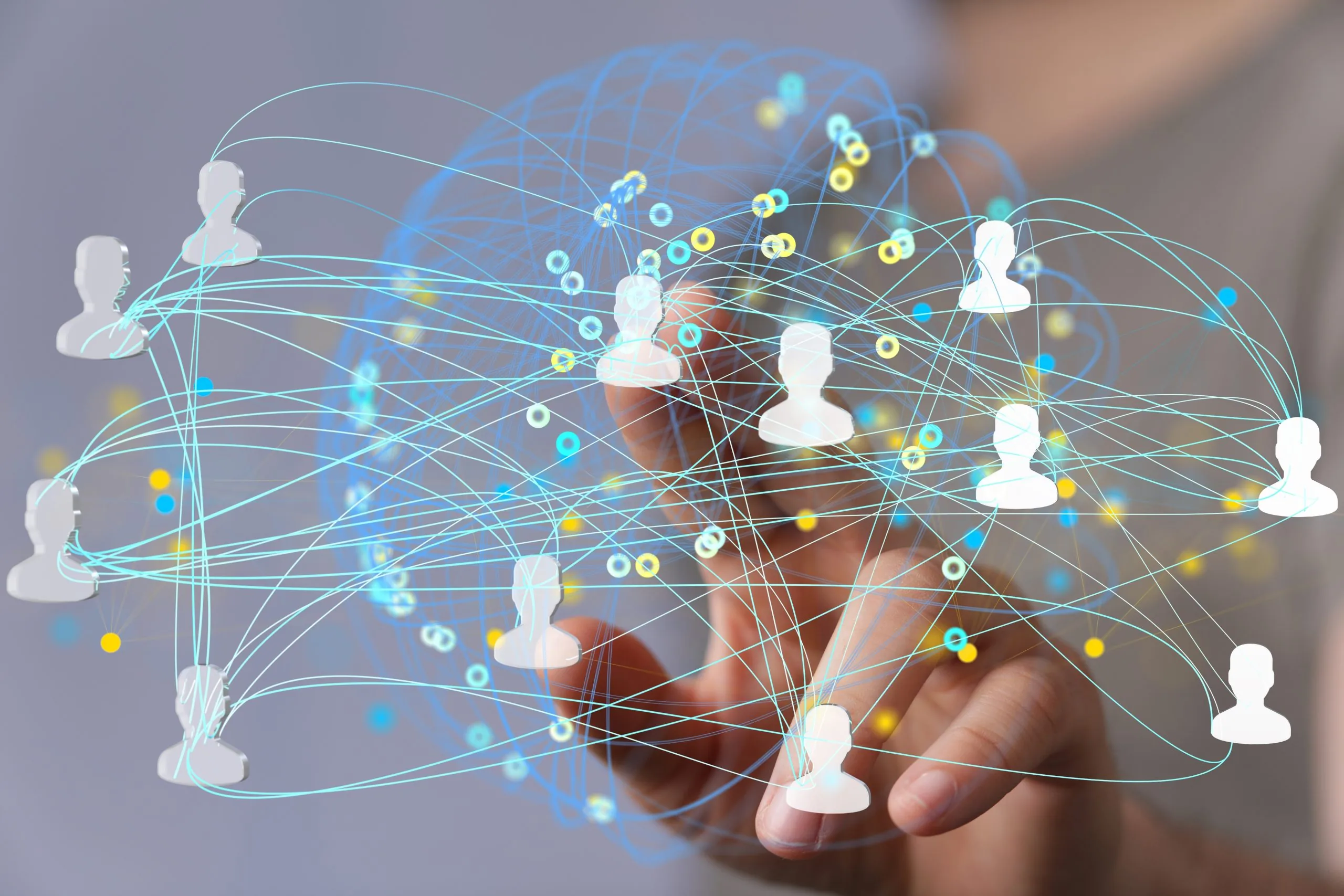 A hand reaching forward, touching virtual icons of connected people, with blue and yellow lines representing a digital network or social connections on a transparent screen.