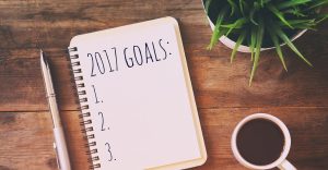 A notebook with 2017 goals written on it, accompanied by a pen and a cup of coffee.